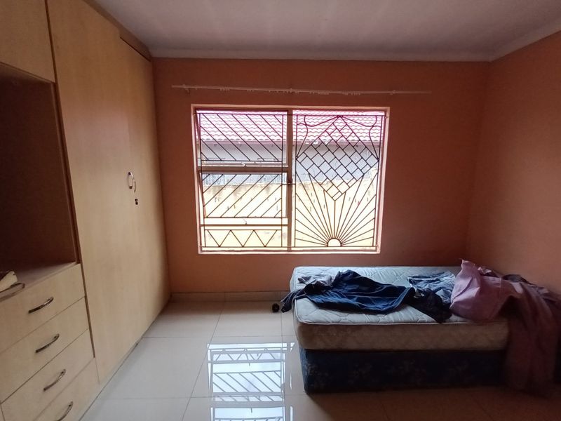 A bedroom featuring tiled flooring, a built-in wardrobe, and a window fitted with security burglar bars.