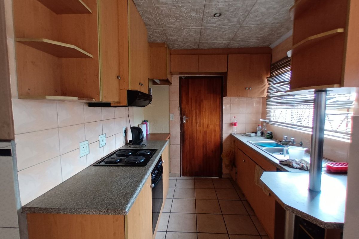 A functional kitchen featuring wood-look cabinetry, laminate countertops, an integrated electric hob and oven, and tiled flooring with a tiled backsplash.