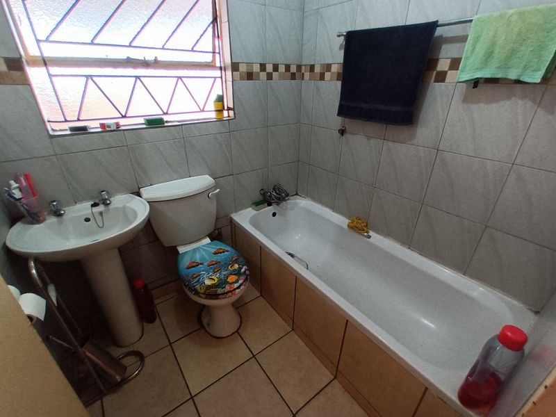 A functional bathroom featuring a pedestal basin, toilet, and bathtub with tiled walls and flooring, complemented by a window with security bars.