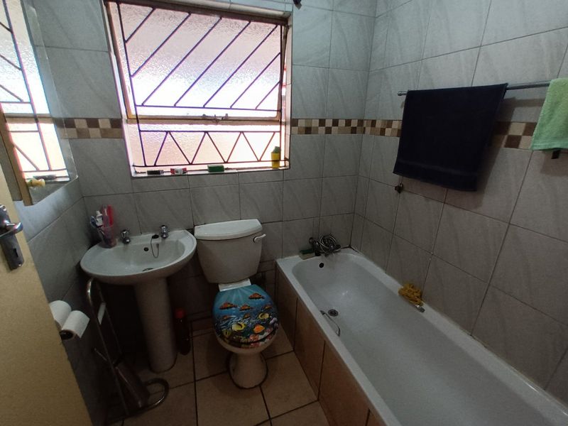 A functional bathroom featuring a pedestal basin, toilet, and bathtub with tiled walls and flooring, requiring cosmetic updates to modernize the space.