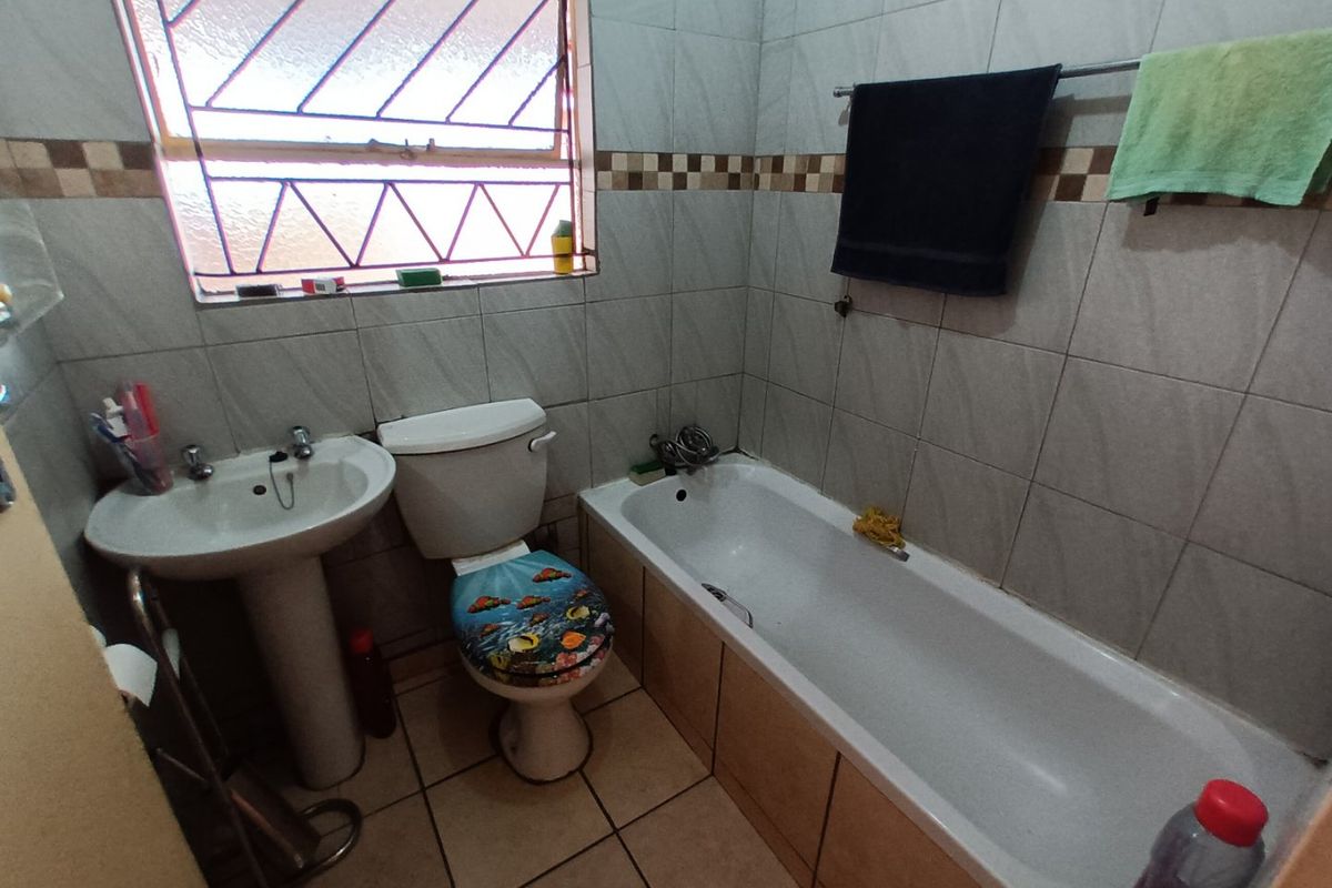 A functional bathroom featuring a pedestal basin, toilet, and bathtub with tiled walls and flooring, including a window with security bars.