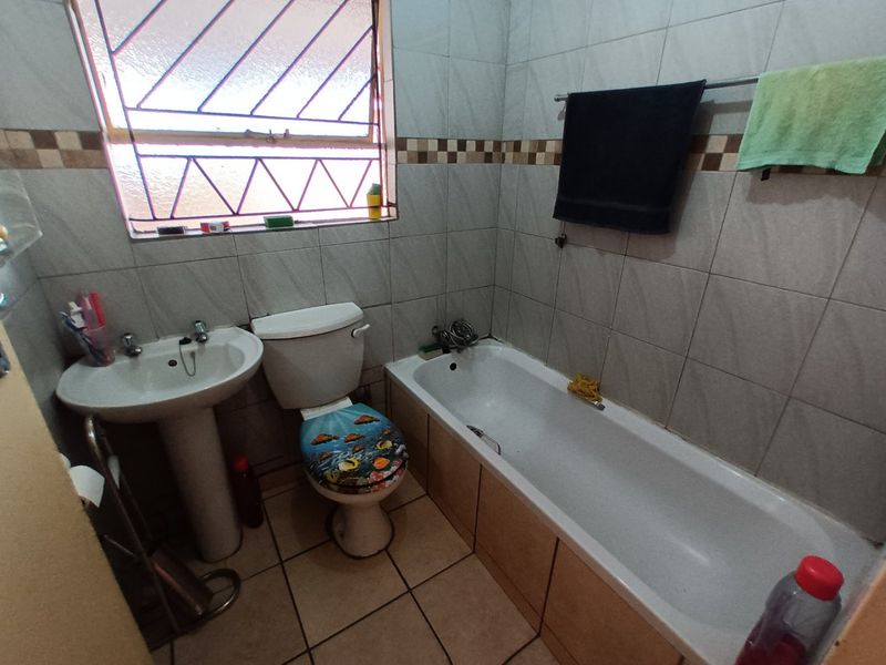A functional bathroom featuring a pedestal basin, toilet, and bathtub with tiled walls and flooring, including a window with security bars.