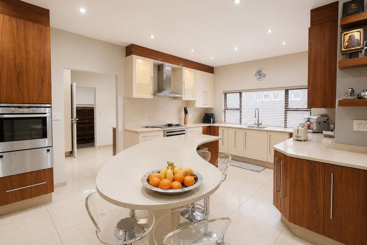 Modern kitchen featuring wood-tone and cream cabinetry, stone countertops, a curved breakfast bar, built-in oven, and recessed lighting with an adjacent scullery area.
