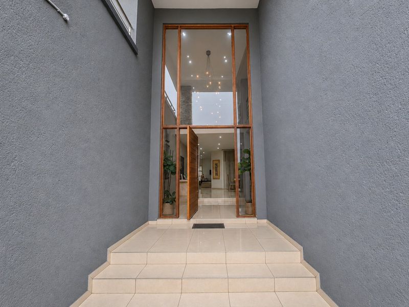 A modern, double-volume entrance featuring a large glass-paneled door, tiled steps, and contemporary textured exterior walls, providing a grand and welcoming arrival.