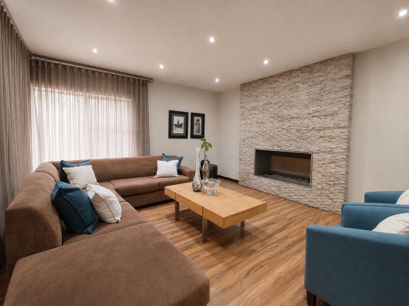 A well-maintained living room featuring a modern stone-clad fireplace, recessed downlighting, and warm-toned laminate timber flooring.