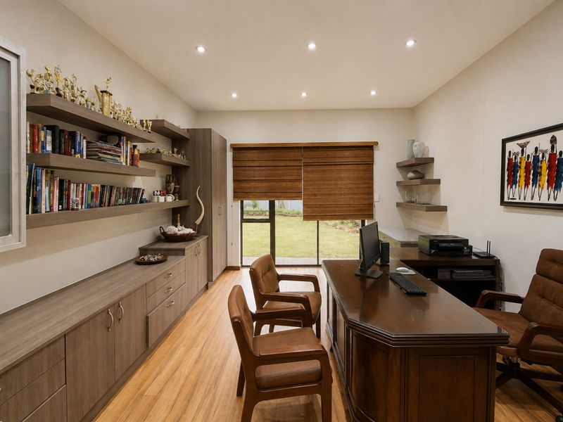 A well-appointed home office featuring extensive built-in cabinetry, floating shelving, recessed lighting, and direct access to the garden through a sliding glass door.