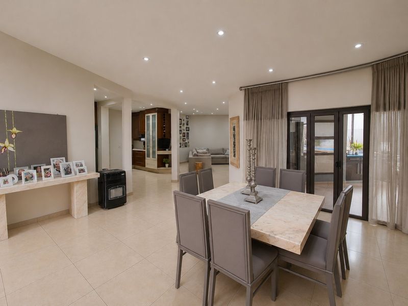 Spacious open-plan living and dining area featuring neutral tiled flooring, recessed lighting, and seamless access to the outdoor patio through sliding glass doors.