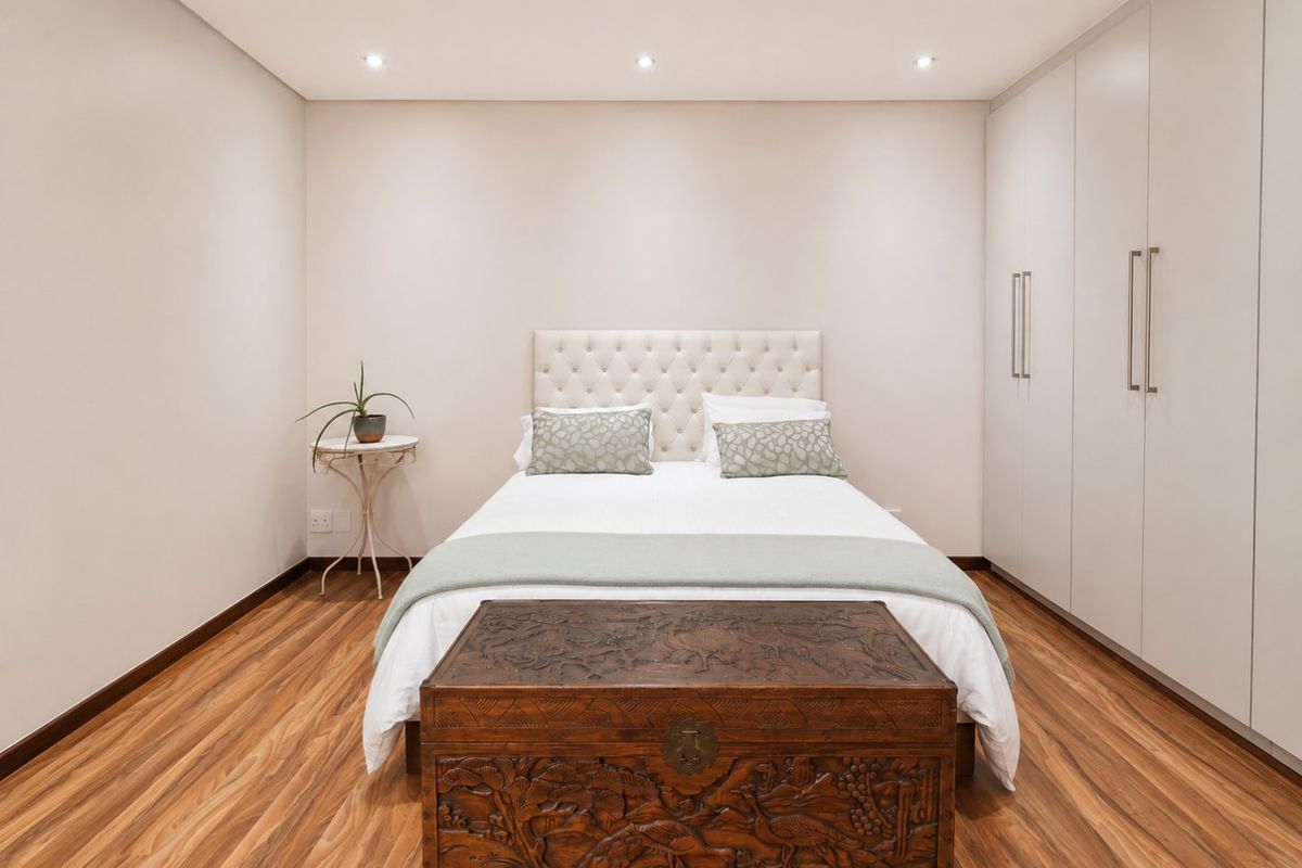 A well-maintained bedroom featuring modern laminate flooring, neutral walls, recessed downlighting, and extensive built-in cupboard storage.