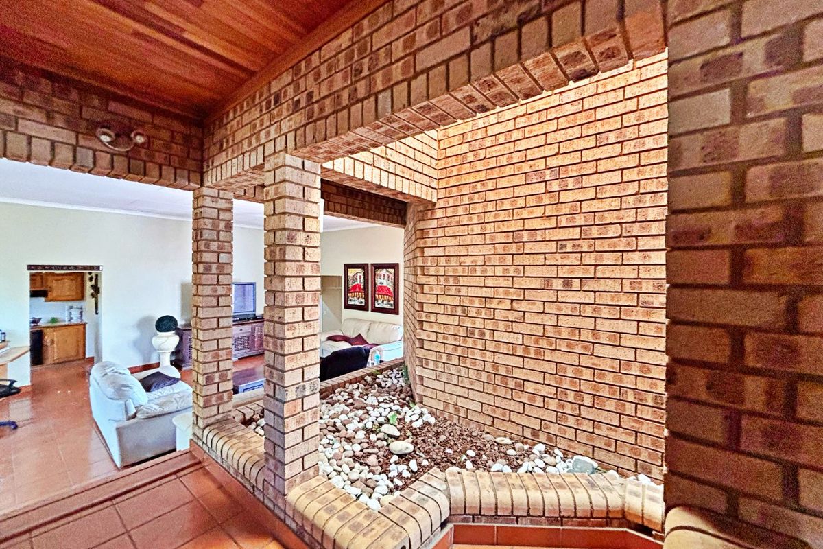Spacious living area featuring a unique internal rock garden, exposed brickwork, timber ceiling, and terracotta floor tiles, creating a distinct architectural character.