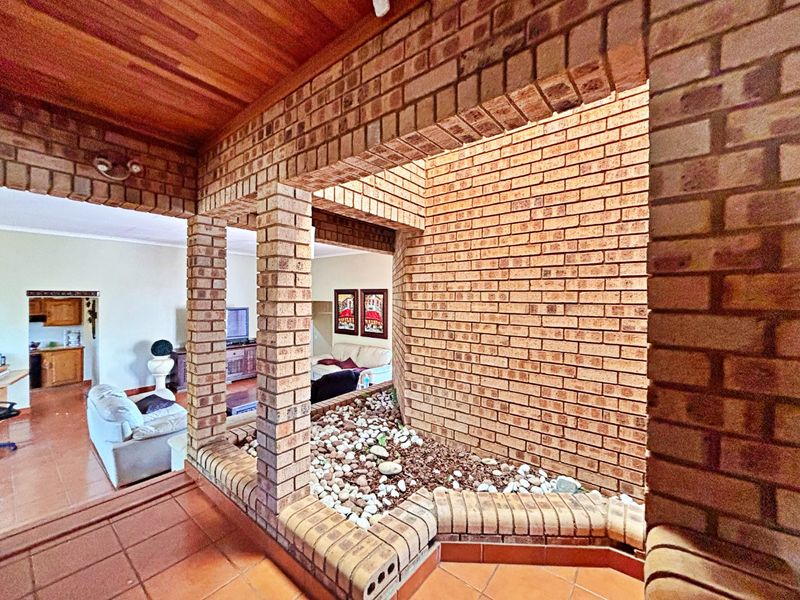 Spacious living area featuring a unique internal rock garden, exposed brickwork, timber ceiling, and terracotta floor tiles, creating a distinct architectural character.