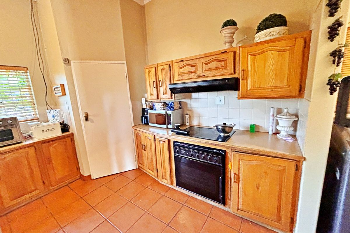 A functional kitchen featuring traditional wooden cabinetry, laminate countertops, a built-in oven with electric hob, and tiled flooring.