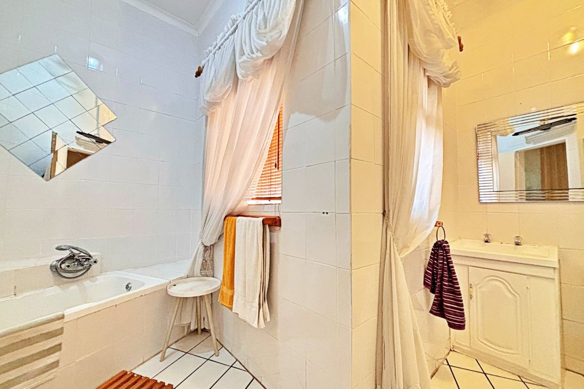 A functional bathroom featuring a built-in bathtub, vanity cabinet with basin, and classic white wall tiling with contrasting floor tiles.