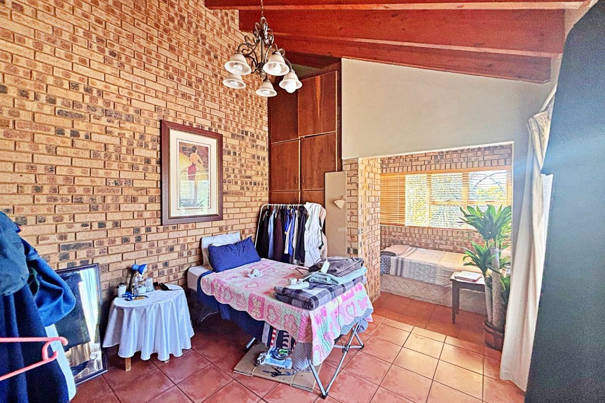 Spacious bedroom featuring exposed brick walls, high timber-beamed ceilings, tiled flooring, and built-in wooden cabinetry with an adjoining alcove area.