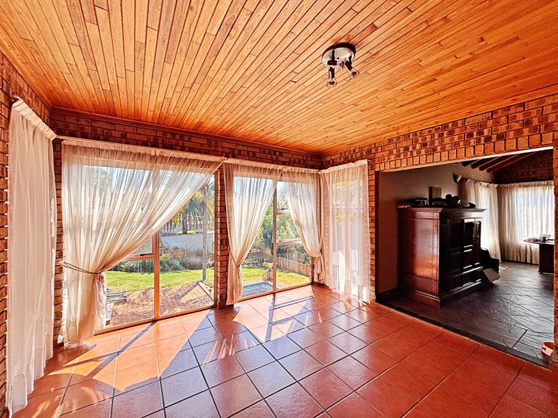Spacious living area featuring exposed brick walls, warm timber ceiling, and terracotta tiled flooring with large sliding doors providing access to the garden.