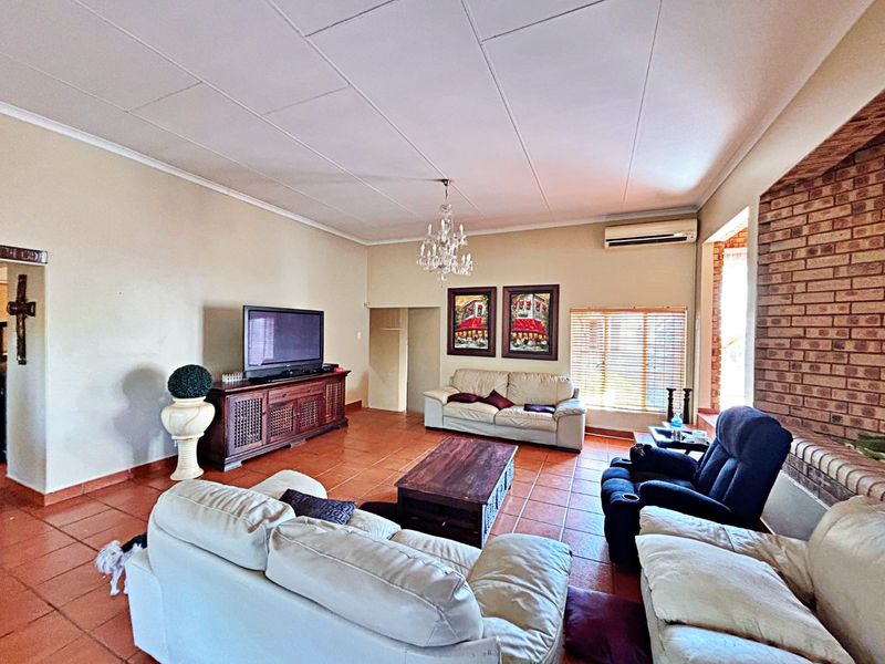 Spacious living room featuring terracotta tiled flooring, an exposed brick accent wall, and a split-system air conditioning unit.