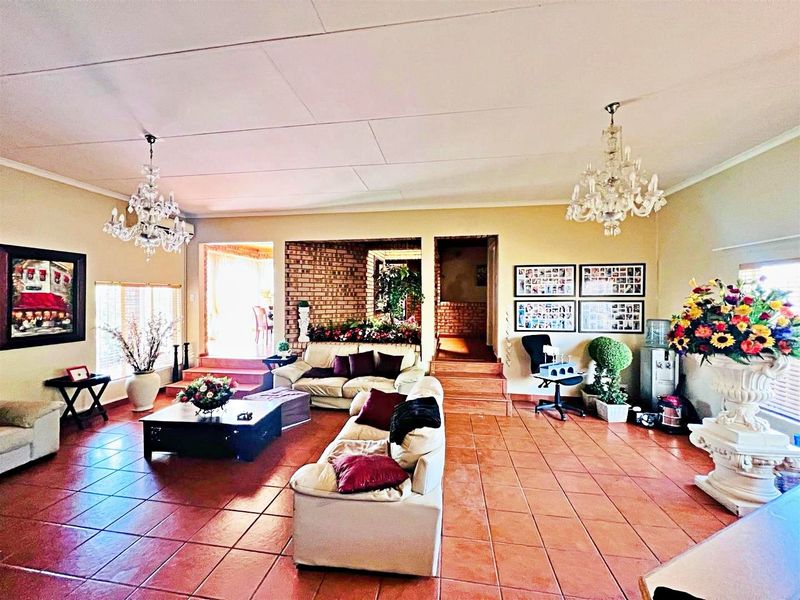 Spacious living area featuring terracotta floor tiles, exposed brick accents, and dual crystal chandeliers, with raised floor levels creating distinct zones.