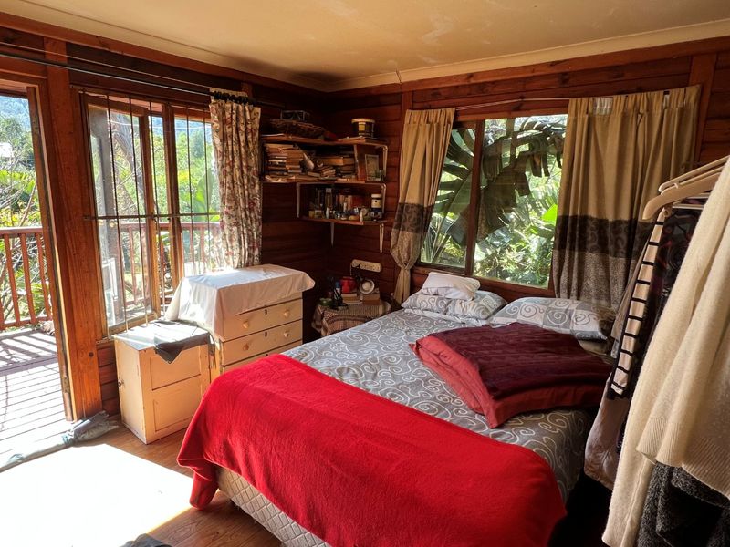 Cozy bedroom featuring rustic timber wall cladding, wooden flooring, and direct access to an outdoor balcony through a sliding glass door.
