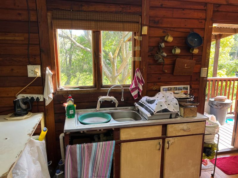 A rustic kitchen area featuring timber wall cladding, a stainless steel double sink, and built-in cabinetry with a view of the garden.