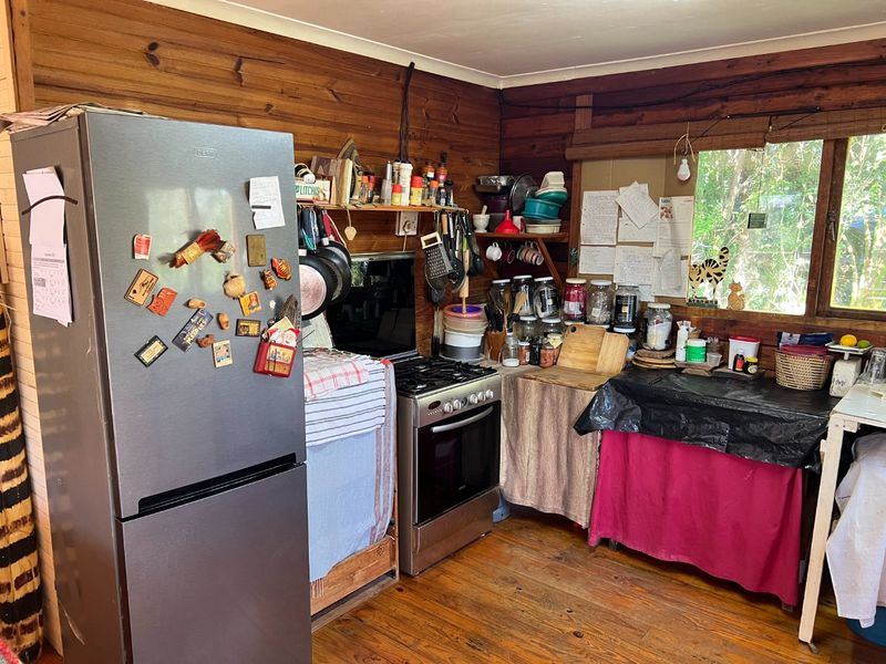 A rustic kitchen featuring timber wall cladding, timber flooring, and a freestanding gas stove with open shelving storage.