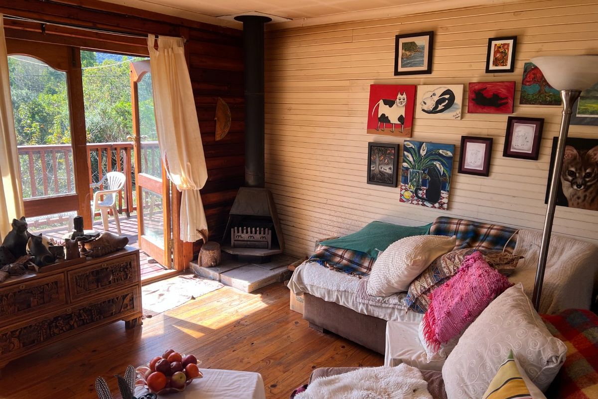 Cozy living room featuring warm timber wall paneling, hardwood floors, and a built-in wood-burning fireplace with direct access to an outdoor deck.