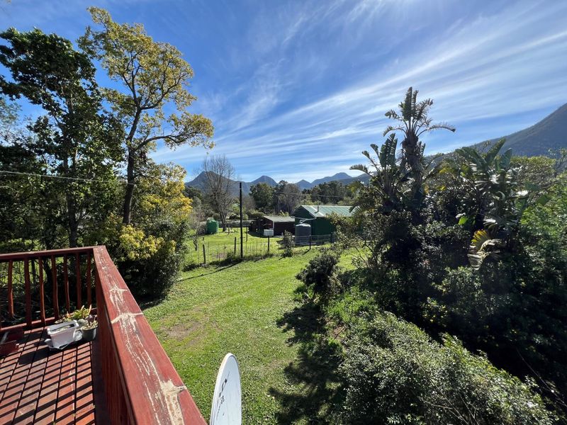 Scenic elevated view overlooking a lush garden, rural outbuildings, and distant mountain ranges from a wooden deck.