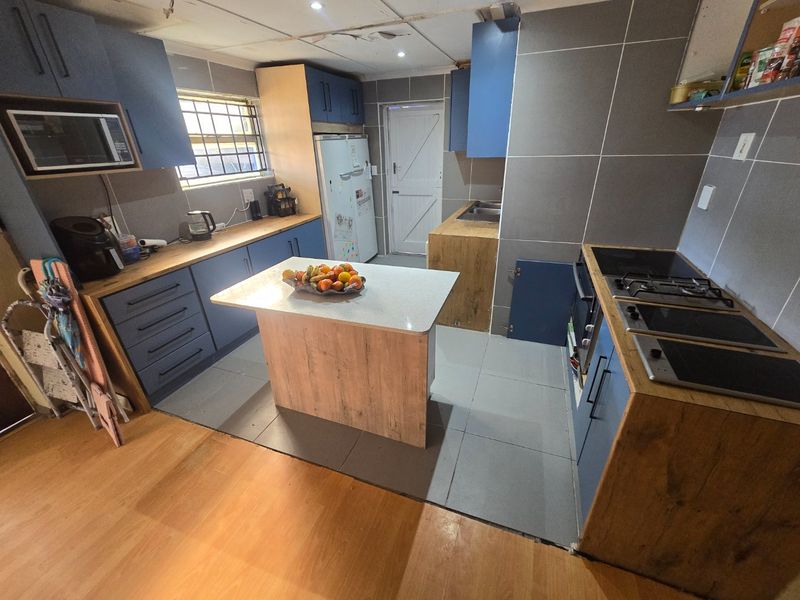 Kitchen featuring blue and wood-tone cabinetry, a central island, and tiled finishes. The space requires maintenance to address ceiling and cabinetry defects.