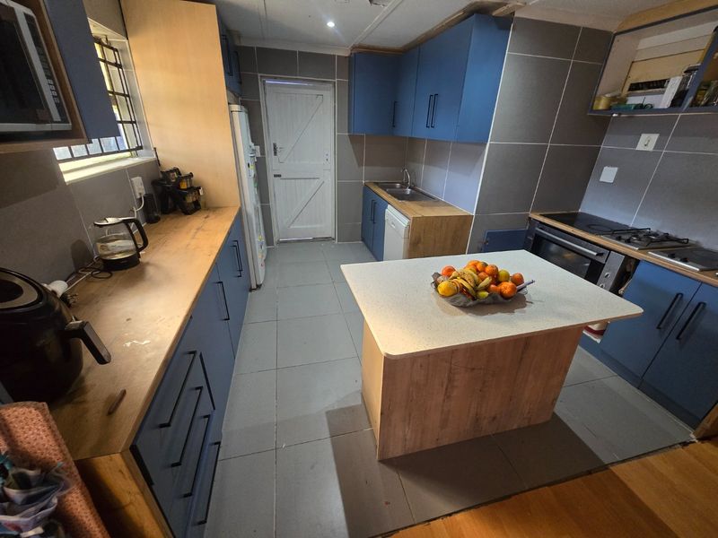 A functional kitchen featuring blue cabinetry, a central island, tiled flooring, and built-in cooking appliances, offering a practical layout for daily meal preparation.