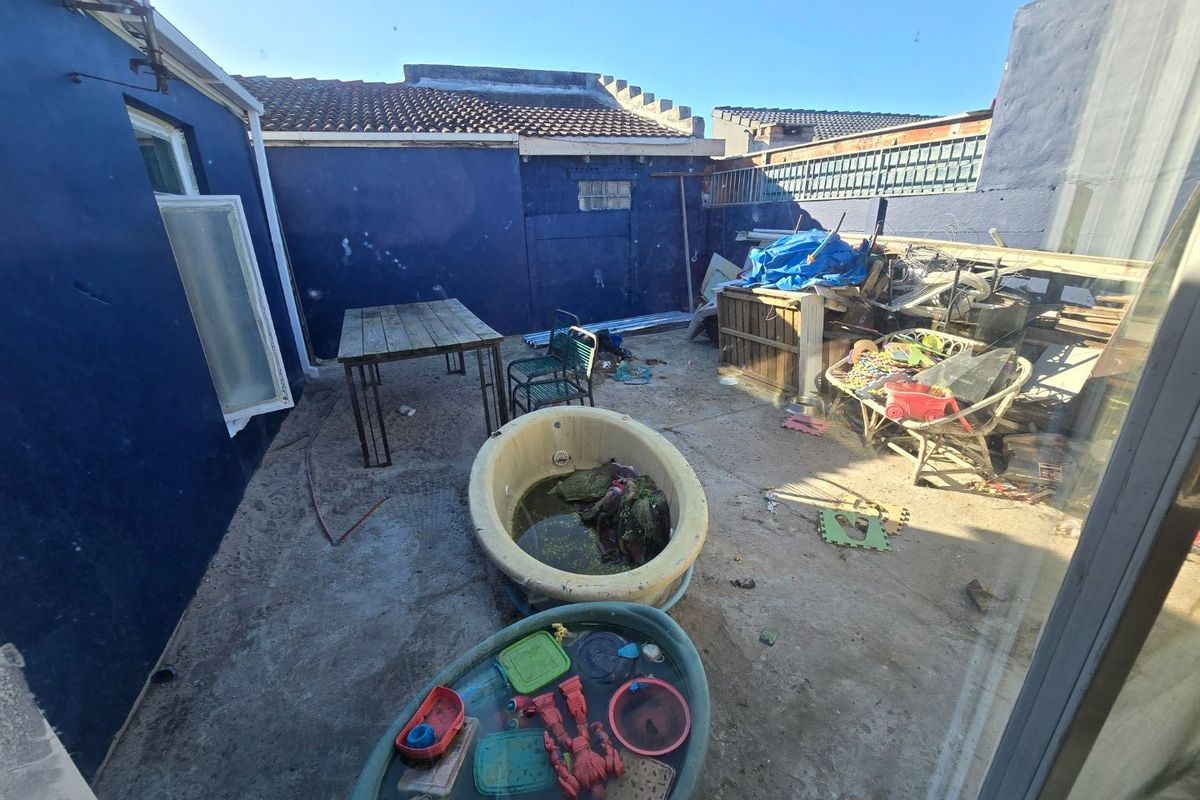 Rear exterior courtyard area featuring concrete paving and boundary walls, currently requiring significant clearing and maintenance to restore the outdoor space.