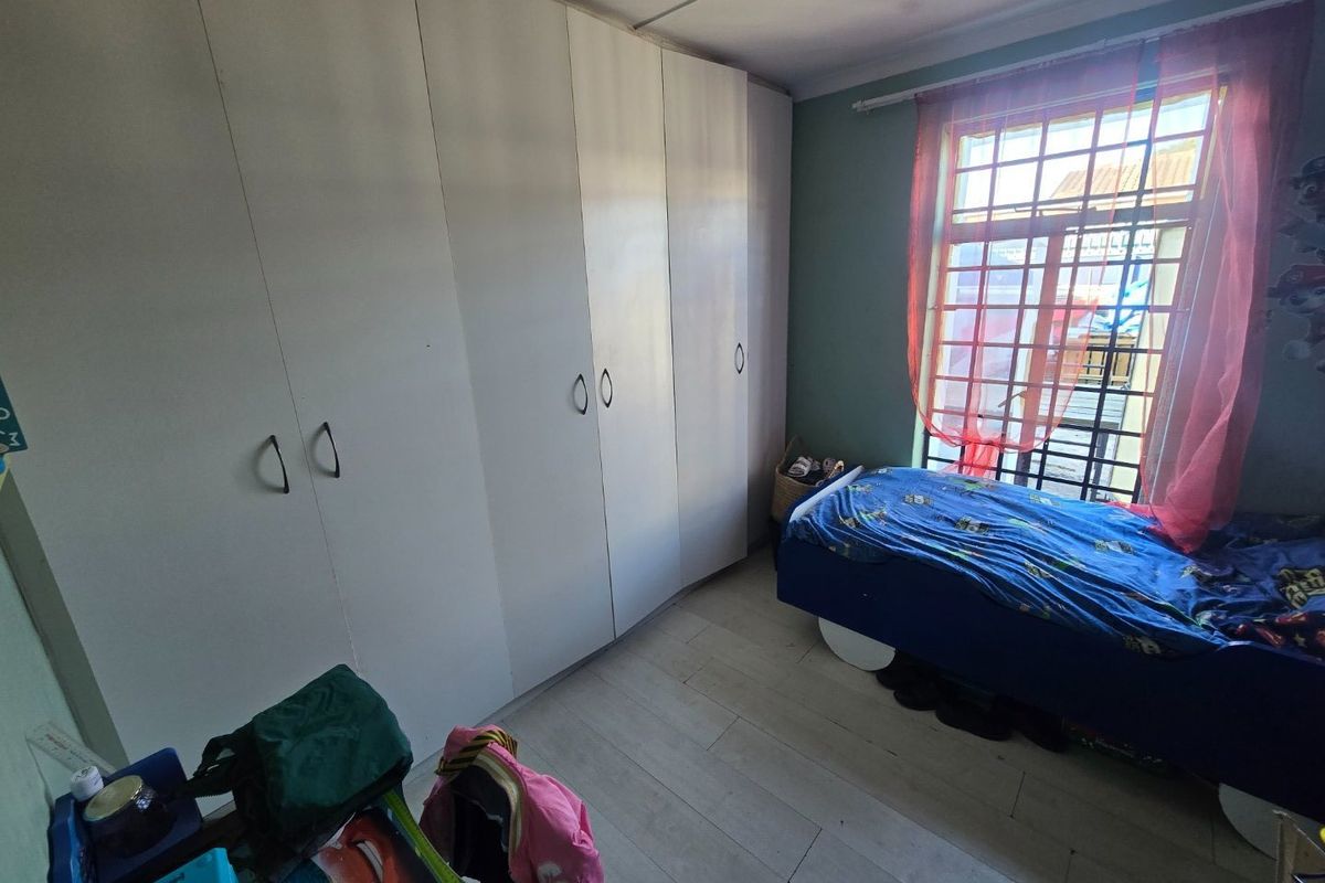 A bedroom featuring built-in cupboards, laminate flooring, and a window fitted with security bars.