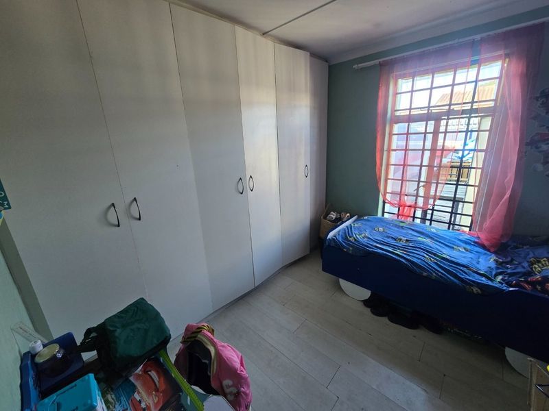 A bedroom featuring built-in cupboards, laminate flooring, and a window fitted with security bars.