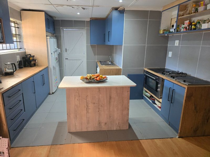 A kitchen featuring blue and wood-tone cabinetry, a central island, and tiled walls, currently requiring repairs to the ceiling and cabinetry finishes.