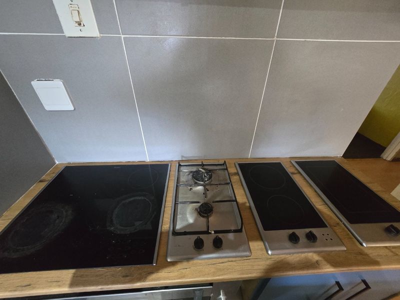 Kitchen workspace featuring a combination of gas and electric cooktops set into a laminate countertop with a grey tiled backsplash.