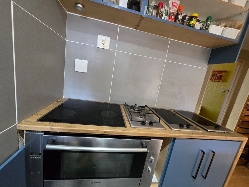 Kitchen cooking area featuring a combination of electric and gas cooktops, built-in oven, tiled backsplash, and wooden countertops with unfinished cabinetry.