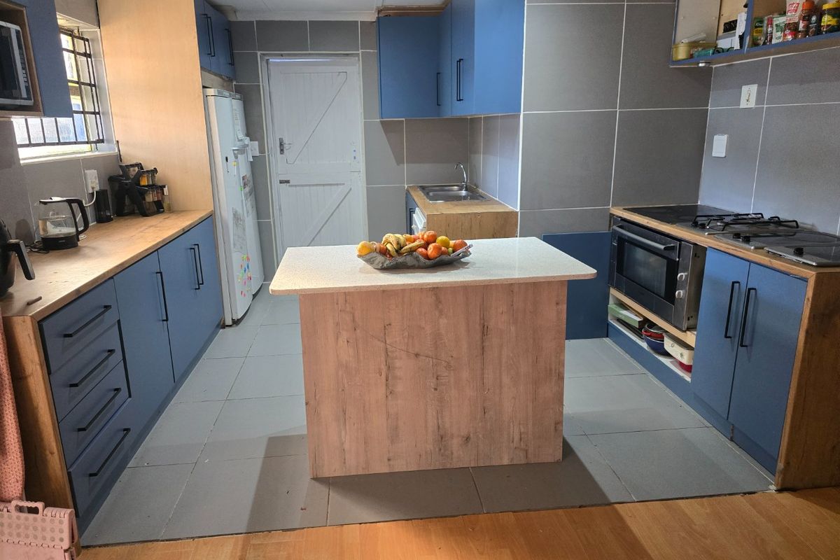 A functional kitchen featuring blue and wood-tone cabinetry, a central island, built-in oven, hob, and tiled finishes throughout.
