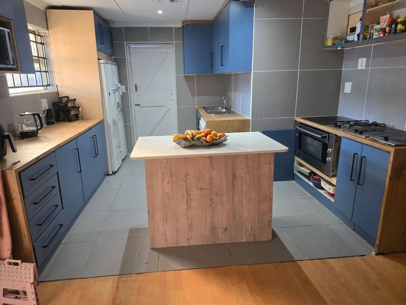A functional kitchen featuring blue and wood-tone cabinetry, a central island, built-in oven, hob, and tiled finishes throughout.
