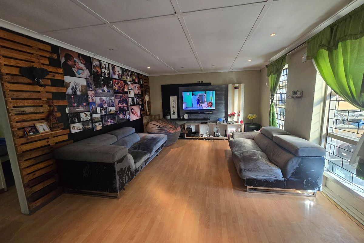 Spacious living room featuring laminate flooring, recessed lighting, and large windows with security bars, offering a versatile area for relaxation and entertainment.