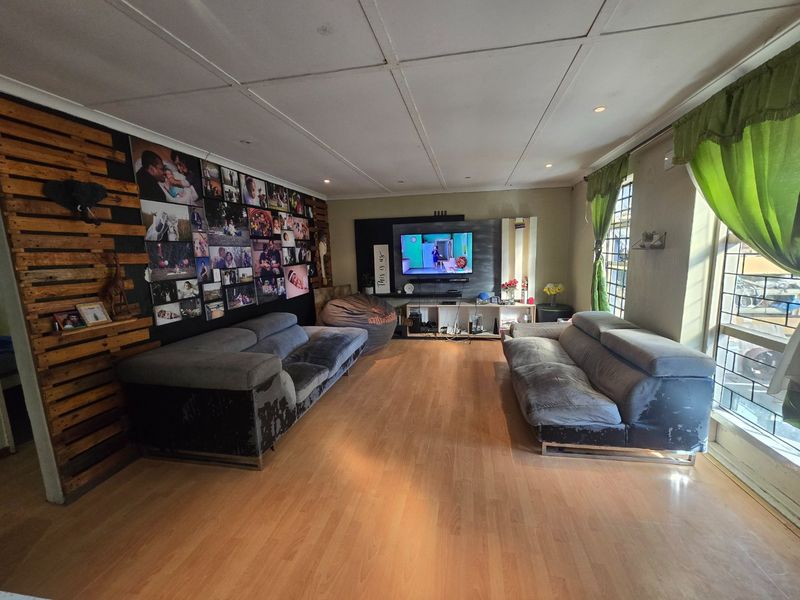 Spacious living room featuring laminate flooring, recessed lighting, and large windows with security bars, offering a versatile area for relaxation and entertainment.