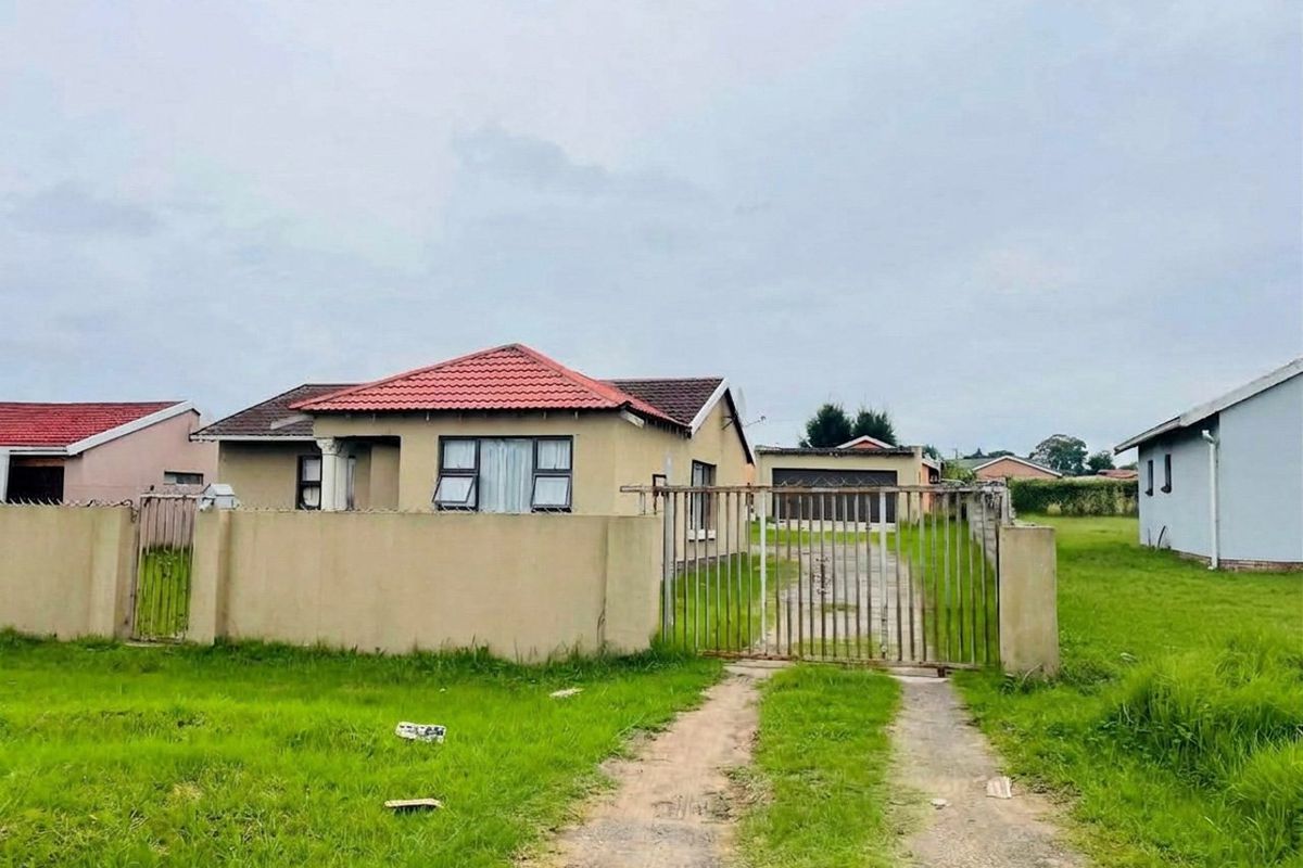 Front view of a detached house featuring a tiled roof, perimeter wall with a metal gate, and a concrete driveway leading to a detached garage.