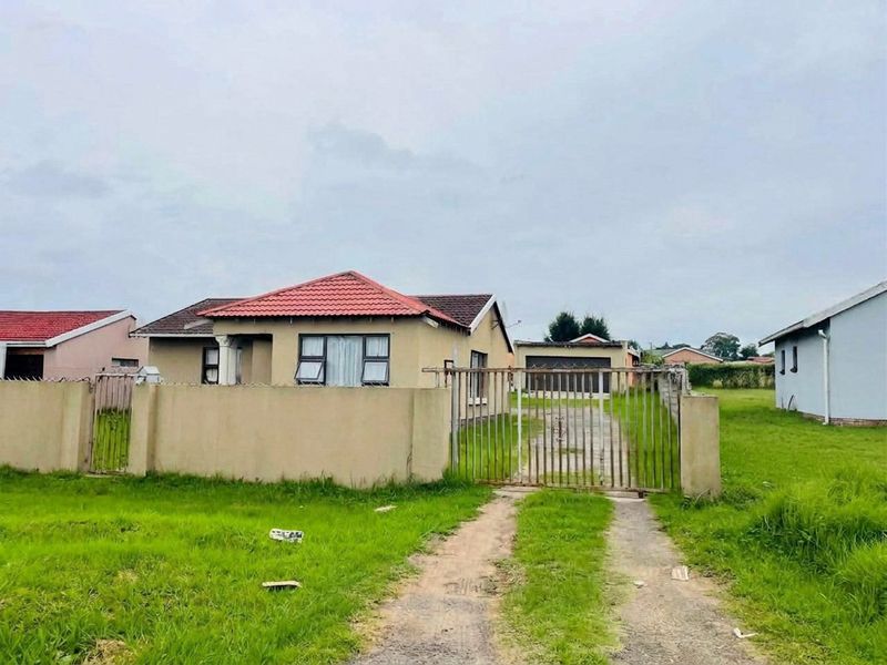 Front view of a detached house featuring a tiled roof, perimeter wall with a metal gate, and a concrete driveway leading to a detached garage.