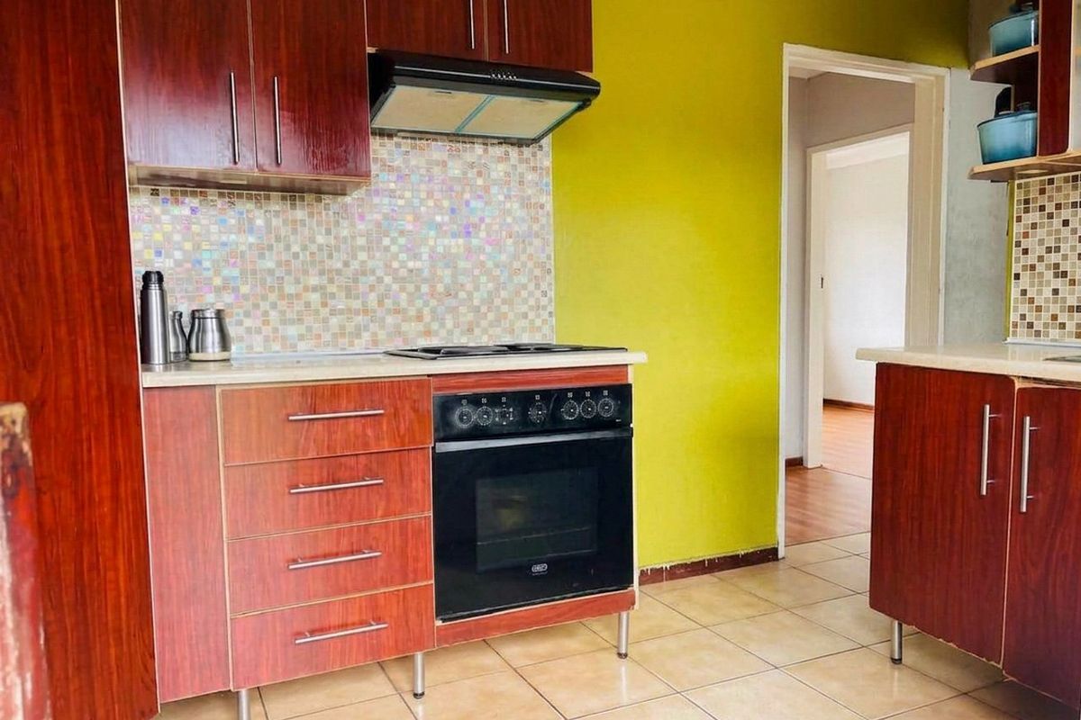 A functional kitchen featuring wood-look cabinetry, a mosaic tile backsplash, built-in oven with hob, and ceramic floor tiles.