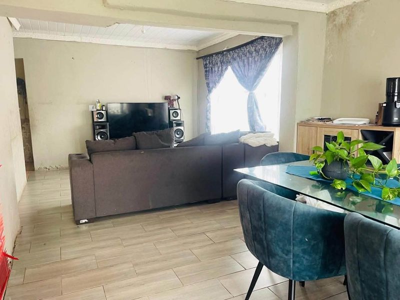 Open-plan living and dining area featuring tiled flooring and large windows, currently showing signs of water damage on the wall and ceiling structure.