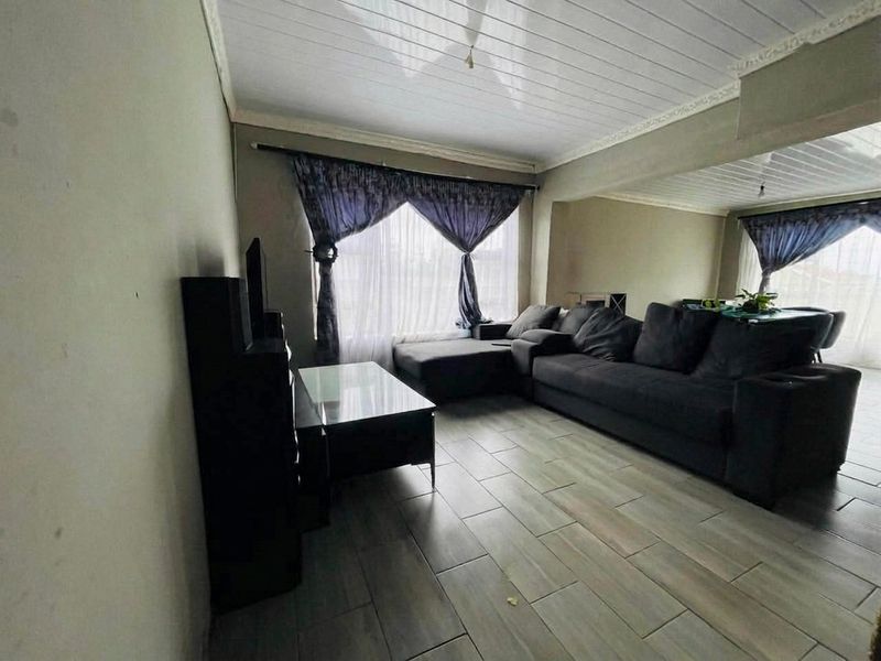 A living room featuring tiled flooring and a panelled ceiling with decorative coving, offering a functional space for relaxation.