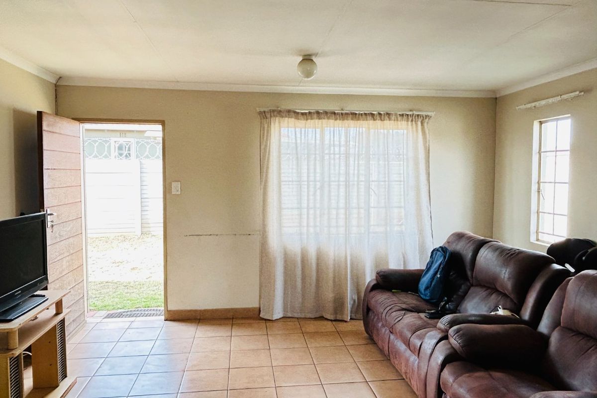 A living room featuring tiled flooring, natural light from a window, and direct access to the exterior through a side door.