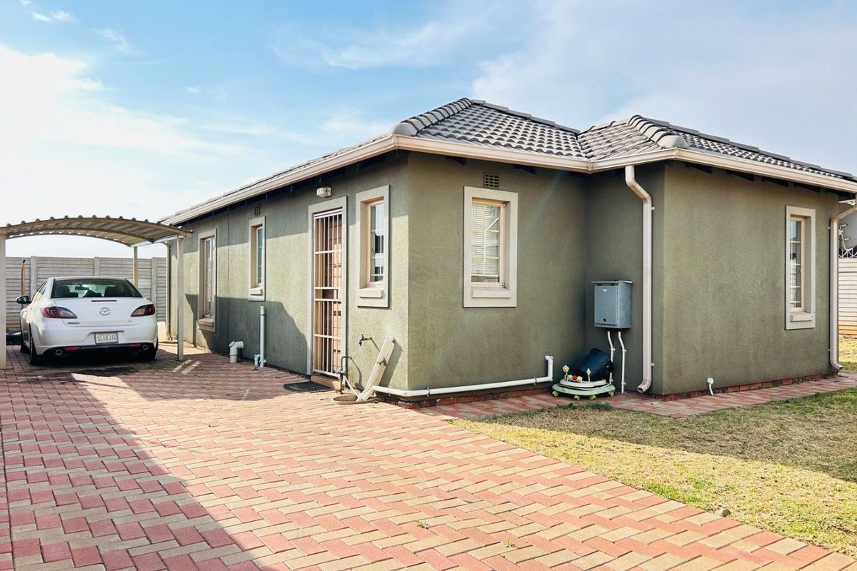 Rear view of the property featuring a paved driveway, carport, plastered exterior walls, and a tiled roof.