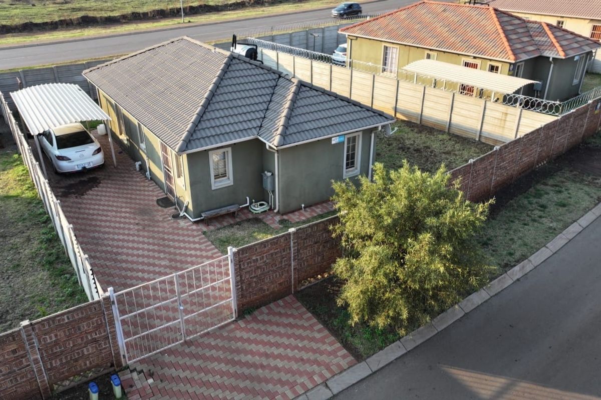 Aerial view of a residential property featuring a tiled roof, paved driveway, carport, and secure perimeter walling with gated access.