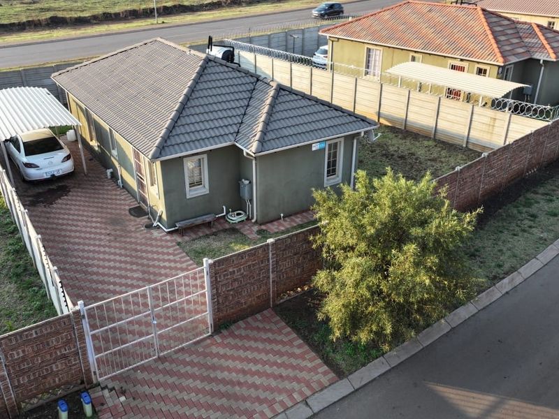 Aerial view of a residential property featuring a tiled roof, paved driveway, carport, and secure perimeter walling with gated access.