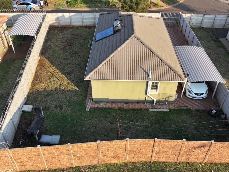 Aerial view of a residential property featuring a tiled roof with solar water heating, a carport, and a fenced garden area.