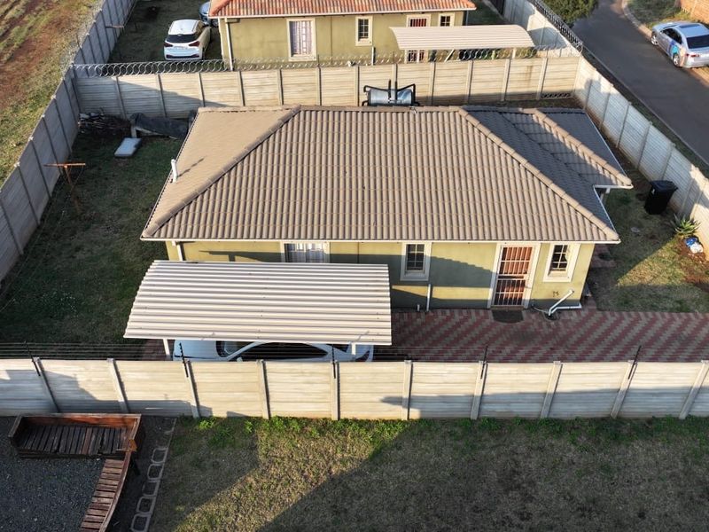 Aerial view of a residential property featuring a tiled roof, carport, paved driveway, and secure precast concrete boundary walling.
