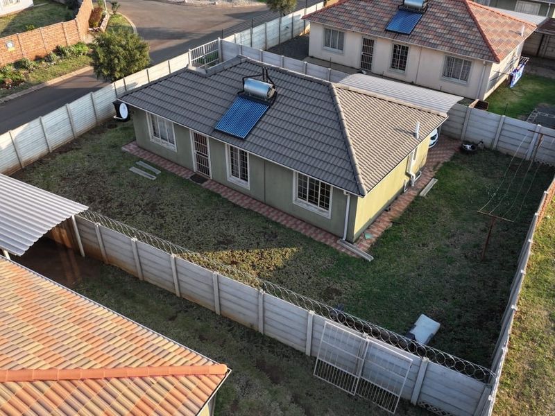 Aerial view of a residential property featuring a tiled roof with a solar water heater, enclosed by precast concrete boundary walls with security fencing.