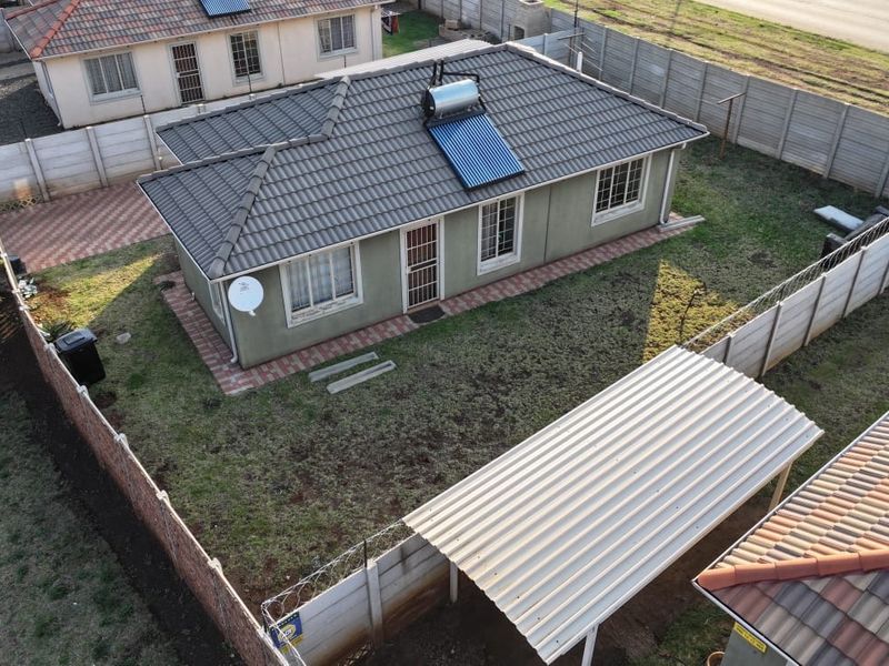 Aerial view of a residential property featuring a tiled roof with a solar water heater, a private garden, and a carport.